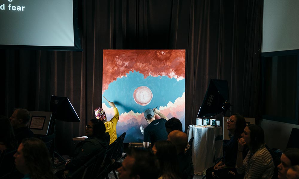 Two Questers work on a large painting in the Quest sanctuary during Sunday service at Quest.