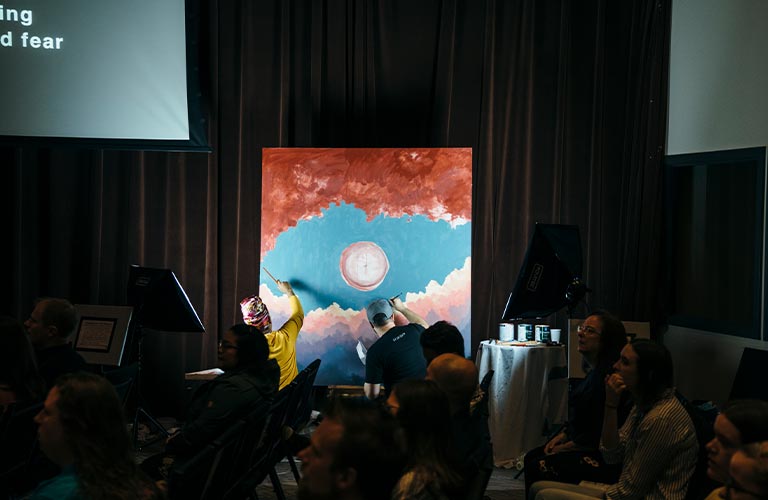 Two Questers work on a large painting in the Quest sanctuary during Sunday service at Quest.