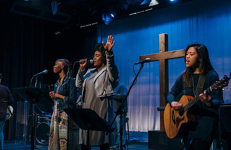 Two Black womena and an Asian American woman lead worship on the Quest sanctuary stage during a Sunday service