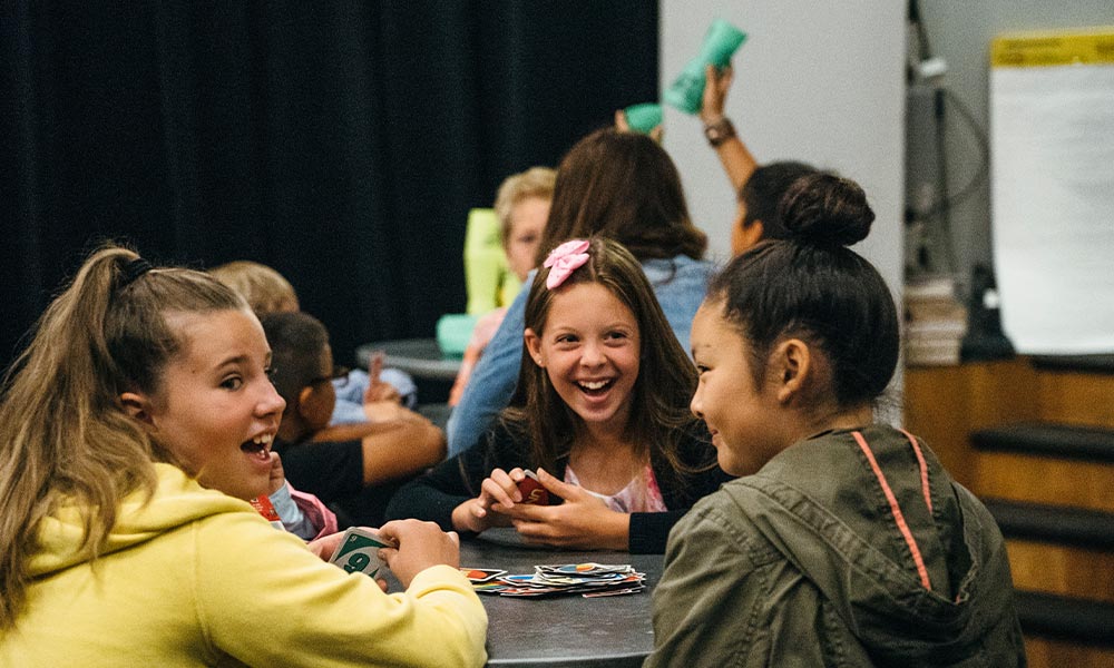 A group of young teenage girls sit around a table playing UNO.
