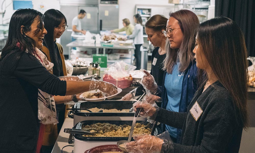 Two lines of volunteers stand on either side of a long table serving Thanksgiving food.